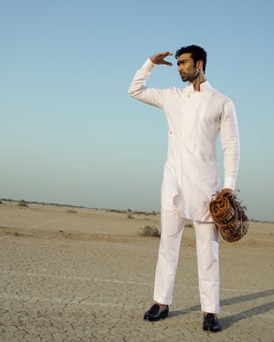 Man in a white traditional outfit standing in a desert landscape with a clear blue sky.