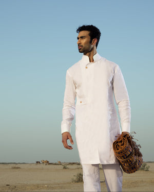 Man in a white traditional outfit holding a leather bag against a desert landscape