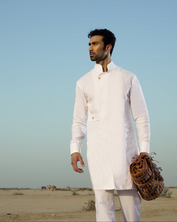 Man in a white traditional outfit holding a leather bag against a desert landscape