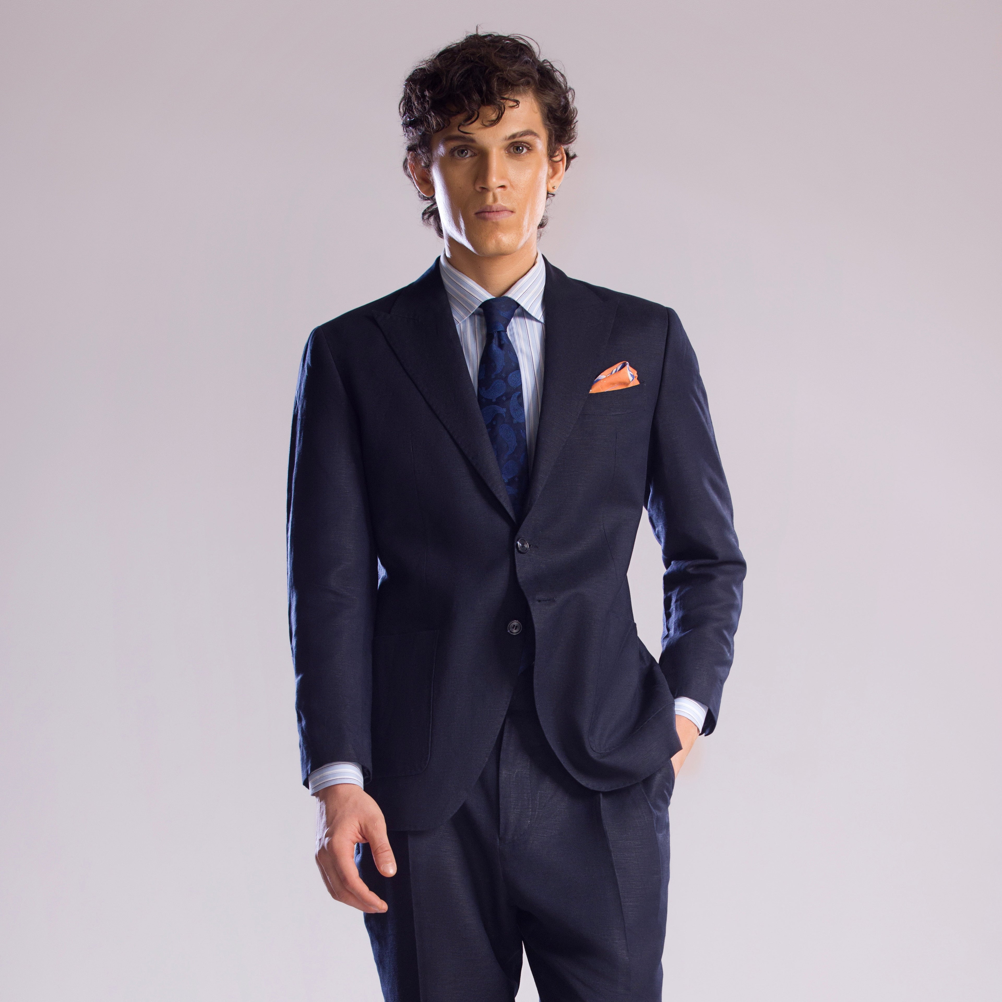Man wearing a navy suit with a white shirt and blue tie on a light gray background
