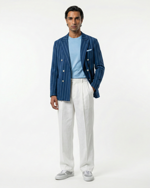 Man wearing a blue striped blazer, light blue shirt, white pants, and gray shoes on a white background