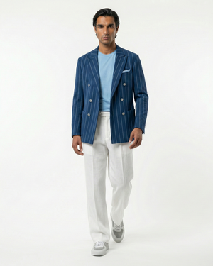 Man wearing a blue pinstripe blazer, light blue shirt, white pants, and gray shoes on a white background