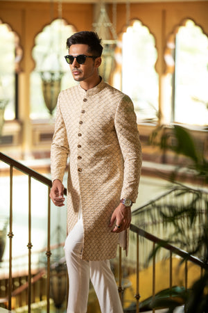 Man wearing a beige kurta with white pants in an indoor setting with decorative elements.