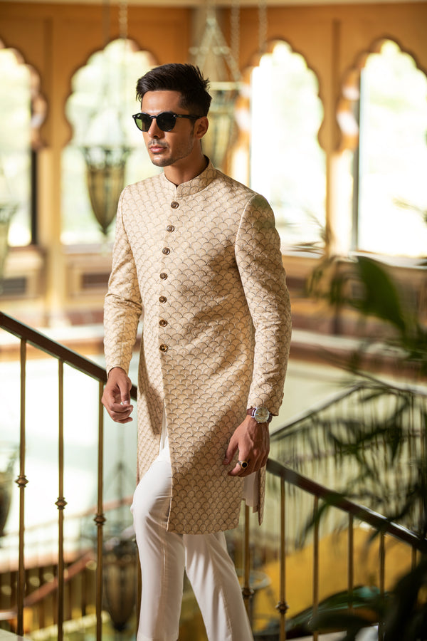 Man wearing a beige kurta with white pants in an indoor setting with decorative elements.