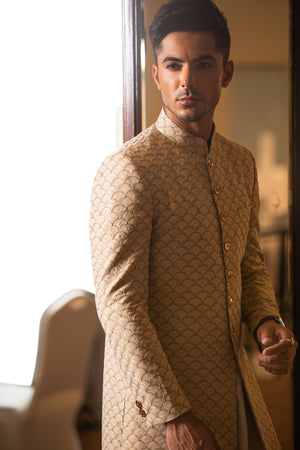 Man wearing a traditional beige sherwani in an indoor setting