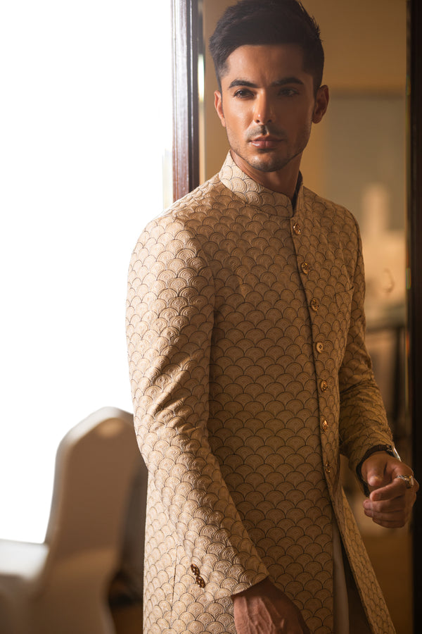 Man wearing a traditional beige sherwani in an indoor setting