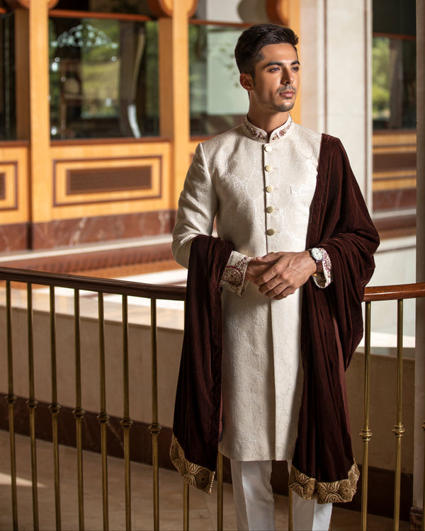 Man wearing a traditional outfit with a brown overcoat in an ornate setting