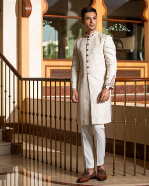 Man in a traditional white sherwani standing in an elegant interior setting.