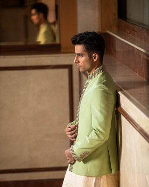 Man in a light green jacket and beige kurta standing indoors.