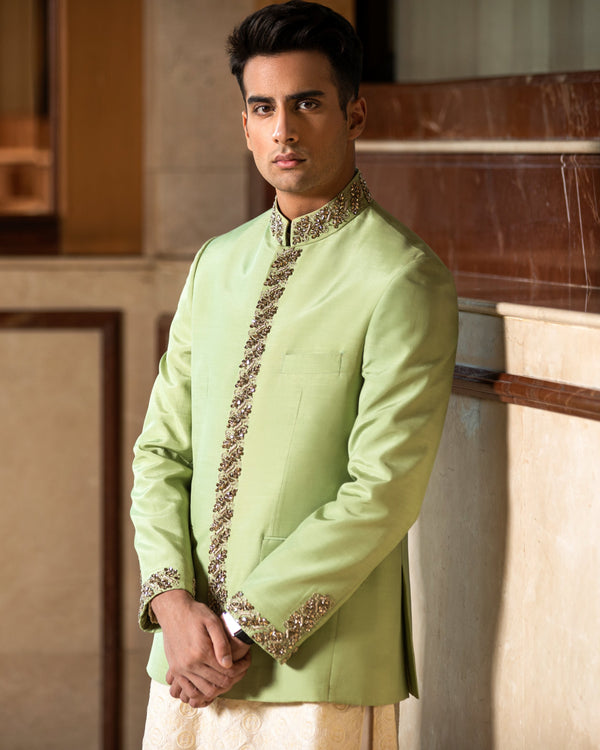 Man wearing a light green traditional outfit with intricate patterns in a room with marble walls.