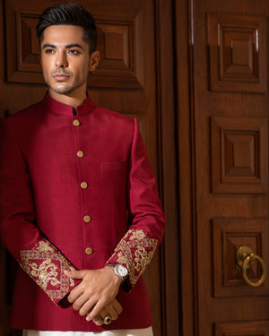 Man wearing a red traditional outfit with white pants in front of a wooden door.