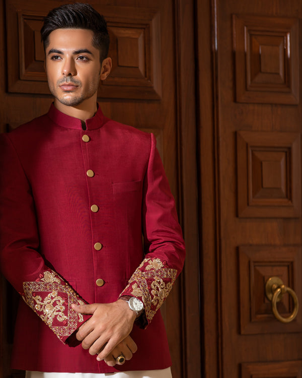 Man wearing a red traditional outfit with white pants in front of a wooden door.