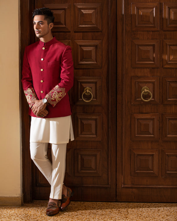 Man in a red traditional outfit standing against a wooden door.
