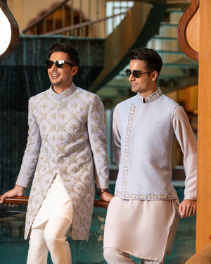 Two men in traditional attire standing in a decorative indoor setting.