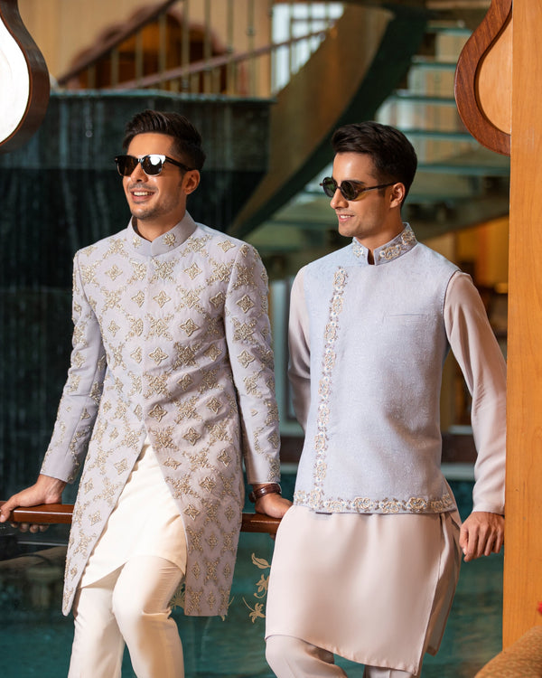 Two men in traditional attire standing in a decorative indoor setting.