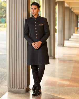 Man wearing a black sherwani standing in an outdoor setting with columns.