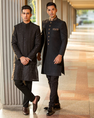 Two men in formal black suits standing in a modern indoor setting.