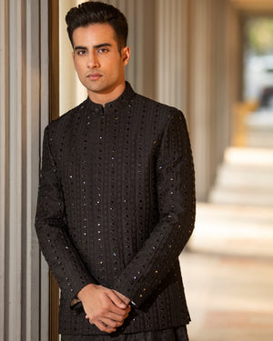 Man wearing a black traditional outfit standing in a hallway.