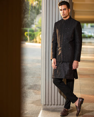Man wearing a traditional black sherwani standing indoors with a blurred background