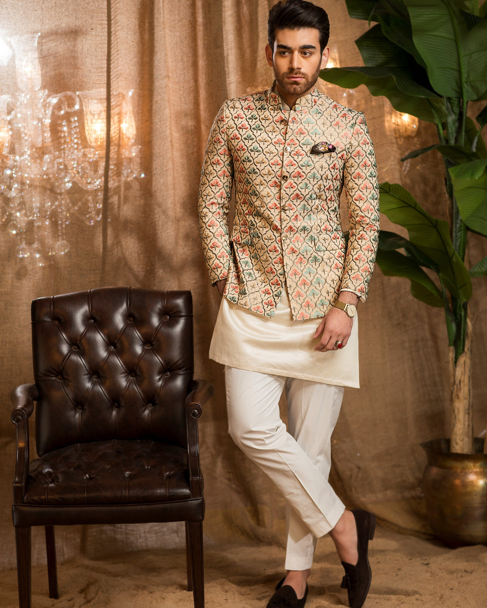 Man in traditional attire standing next to a brown leather chair with decorative elements.