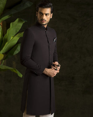Man wearing a black kurta with white pants against a dark background