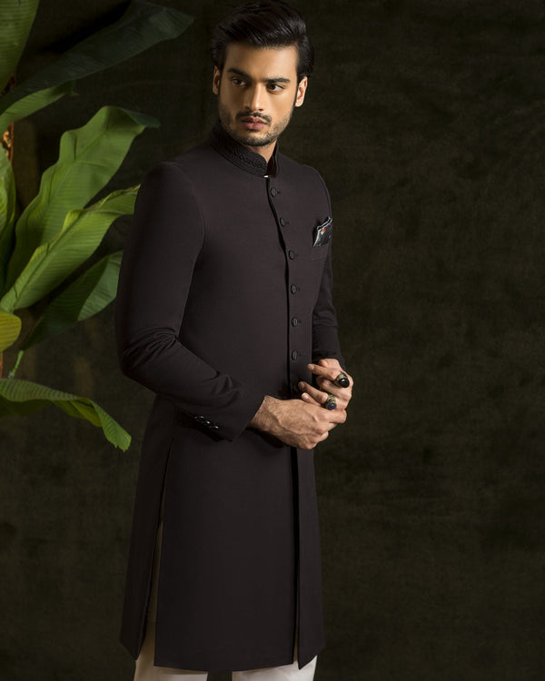 Man wearing a black kurta with white pants against a dark background