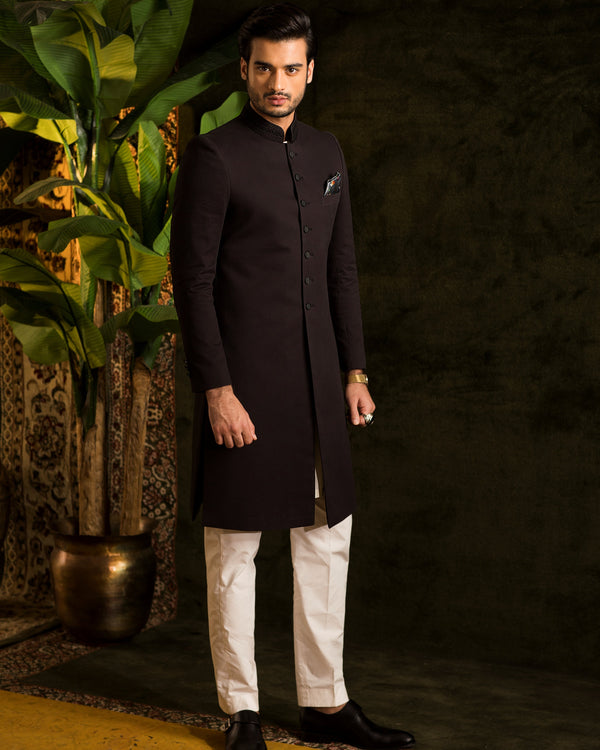 Man wearing a black kurta with white pants standing against a dark background