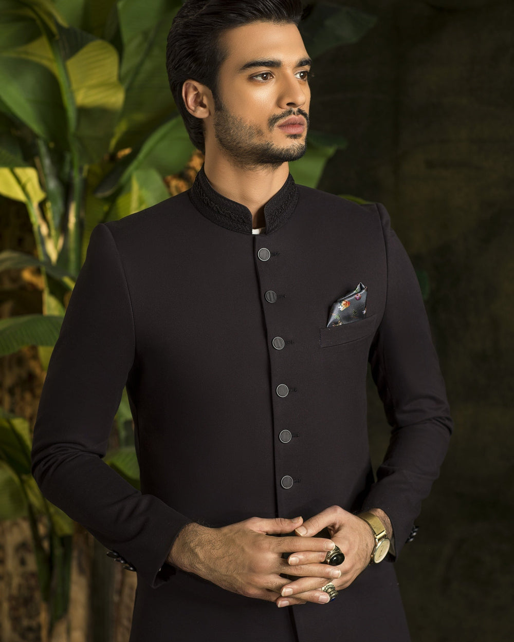 Man wearing a black kurta with white pants standing against a dark background