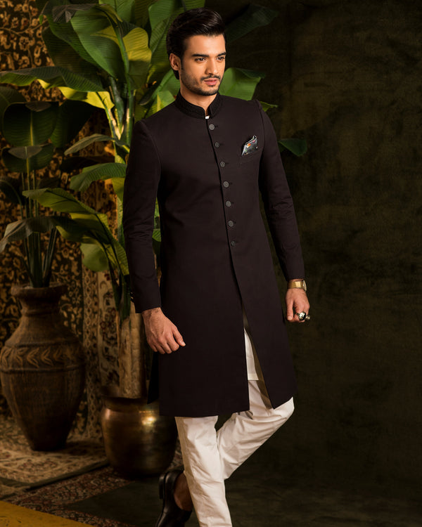 Man wearing a black kurta with white pants in an indoor setting with plants.