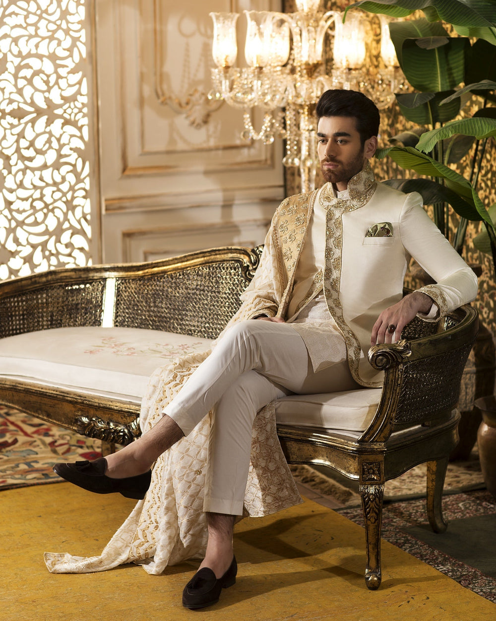 Man in formal attire sitting on an ornate chair in a luxurious room.