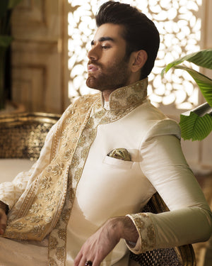 Man wearing a traditional embroidered outfit with a decorative wall in the background