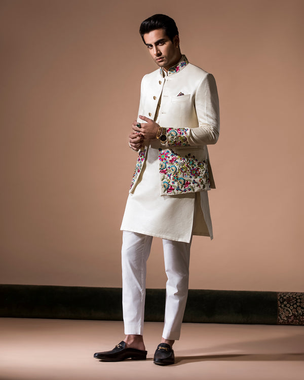 Man wearing a traditional outfit with a floral vest against a beige background