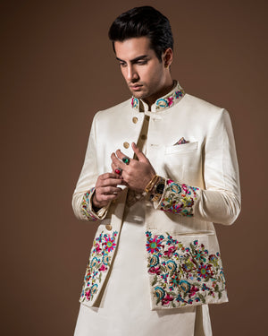 Man wearing a cream-colored embroidered traditional outfit against a brown background
