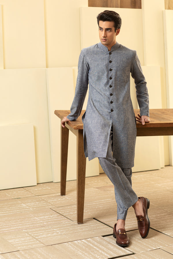 Man wearing a gray kurta with pants standing on a wooden stool against a neutral background