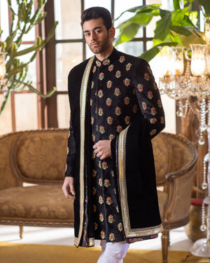 Man wearing a black embroidered sherwani with white pants in an elegant room.