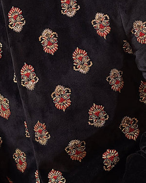 Man in traditional attire sitting on a decorative couch with chandeliers and plants in the background