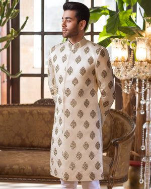 Man wearing a cream kurta with intricate patterns in a stylish room with decorative elements.