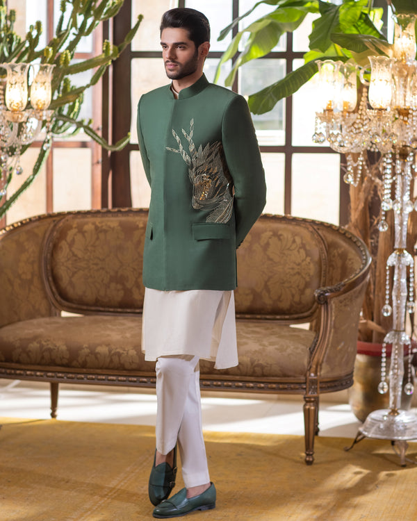 Man in a green kurta with white pants standing in a stylish room with plants and furniture.