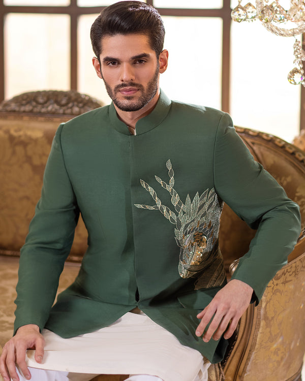 Man wearing a green embroidered jacket sitting on an ornate chair in a decorated room.