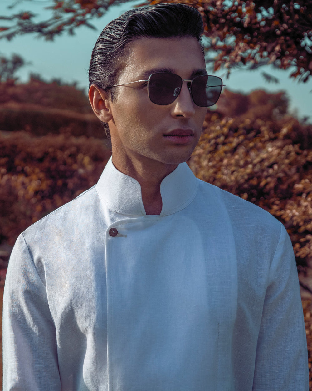 Man wearing sunglasses and a light-colored shirt outdoors with trees in the background