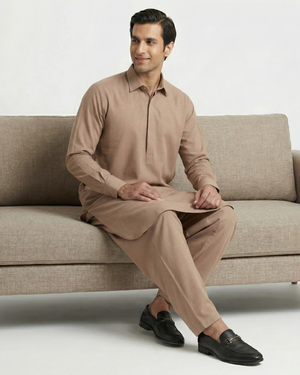 Man sitting on a beige sofa wearing a beige traditional outfit.