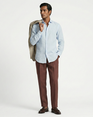 Man wearing a light blue shirt, brown pants, and holding a jacket on a white background