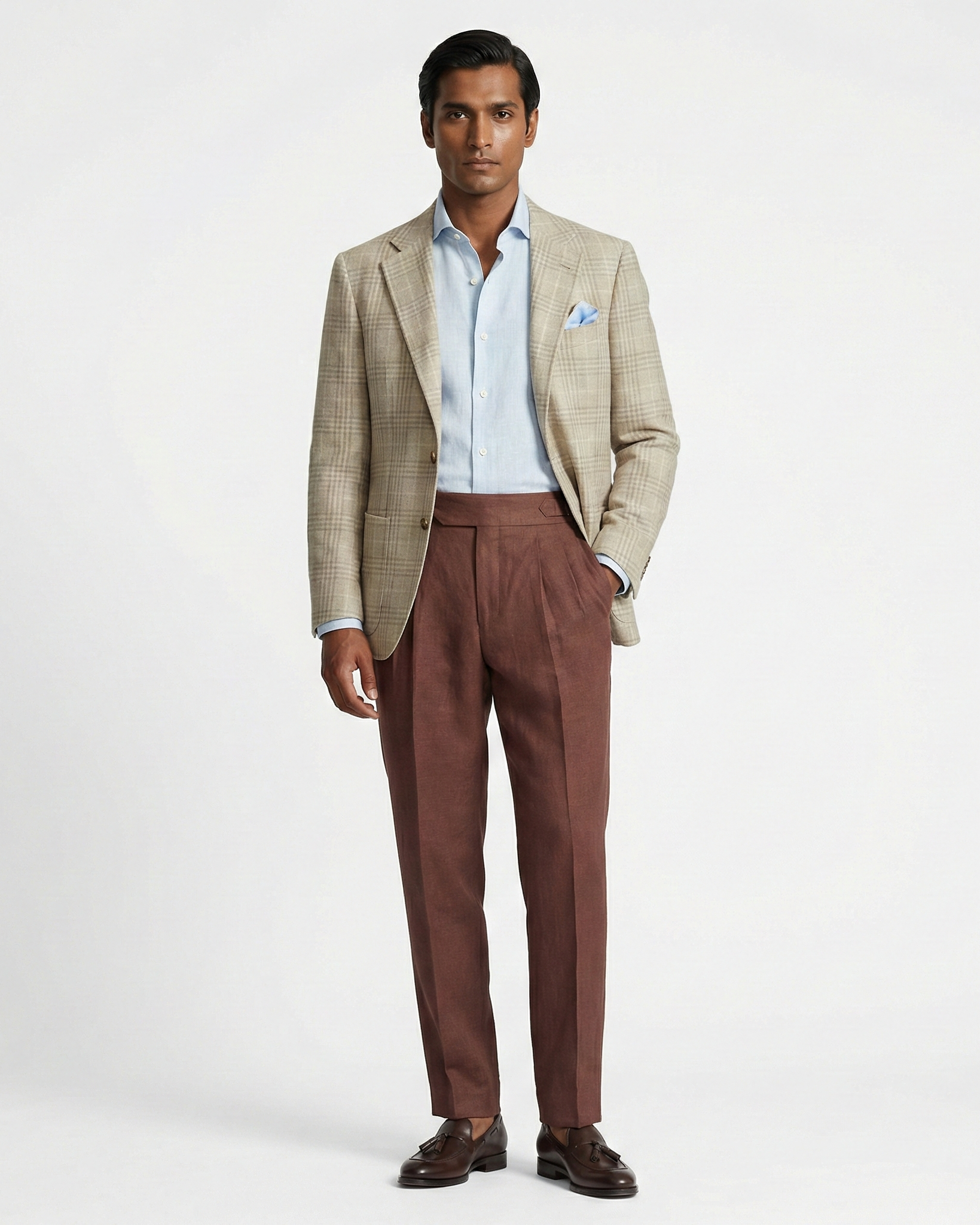 Man wearing a beige checkered blazer, light blue shirt, and brown trousers on a white background
