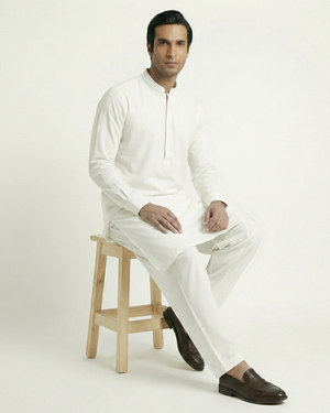 Man sitting on a wooden stool wearing a white traditional outfit against a white background