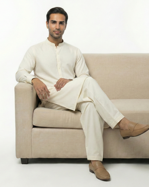 Man sitting on a beige couch wearing a white traditional outfit.