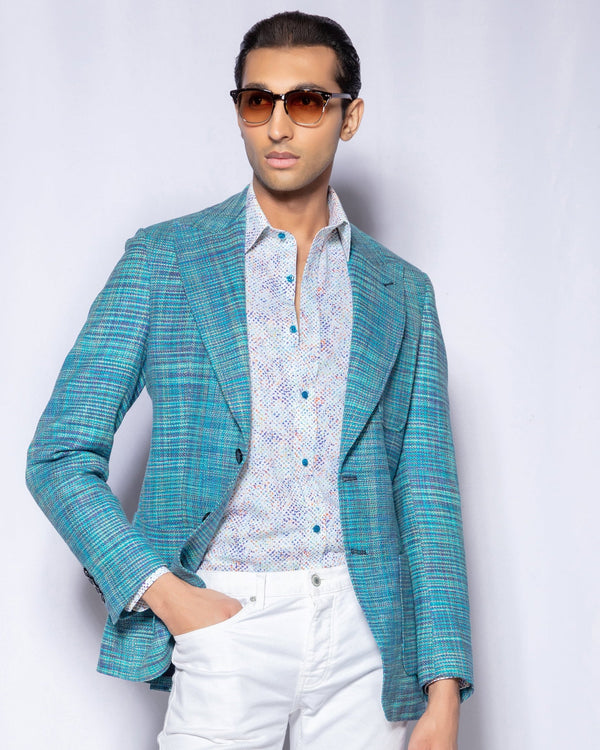 Man wearing a teal blazer, white shirt, and white pants against a plain background