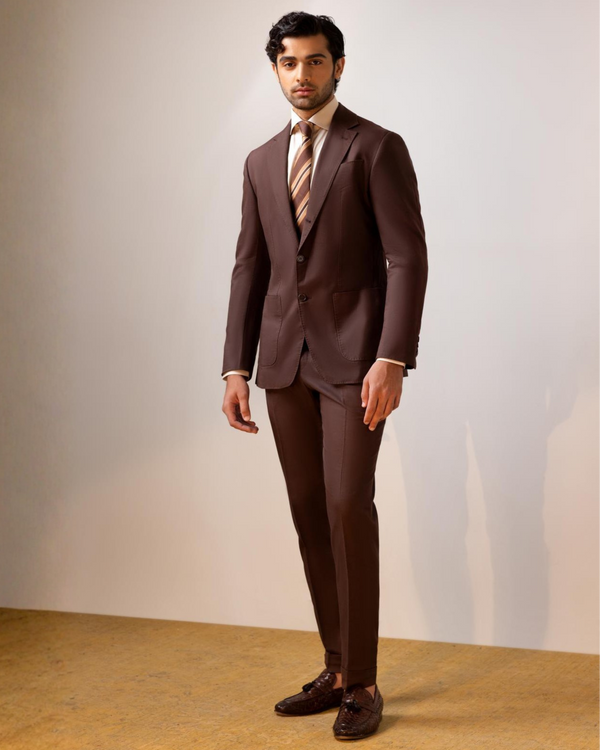 Man wearing a brown suit with a white shirt and tie against a plain background